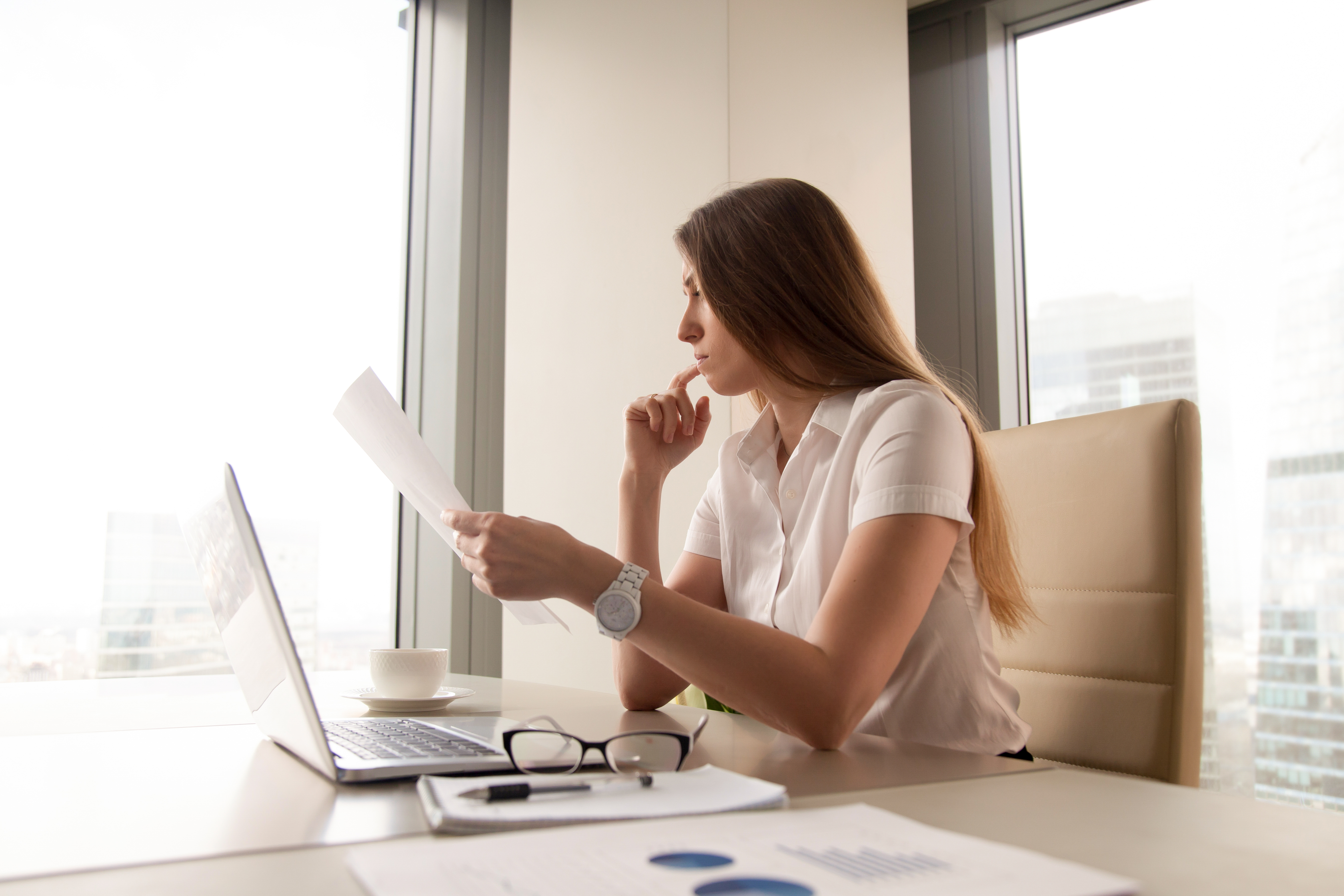 Pensive businesswoman reading document at workplace. Serious female entrepreneur sitting at table and thinking about company financial indicators. Focused woman thoroughly analyzing business letter